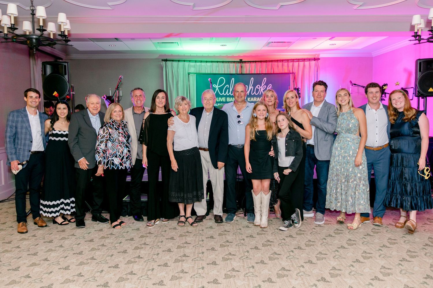 Large group photo of event attendees under colorful lighting in a banquet hall.