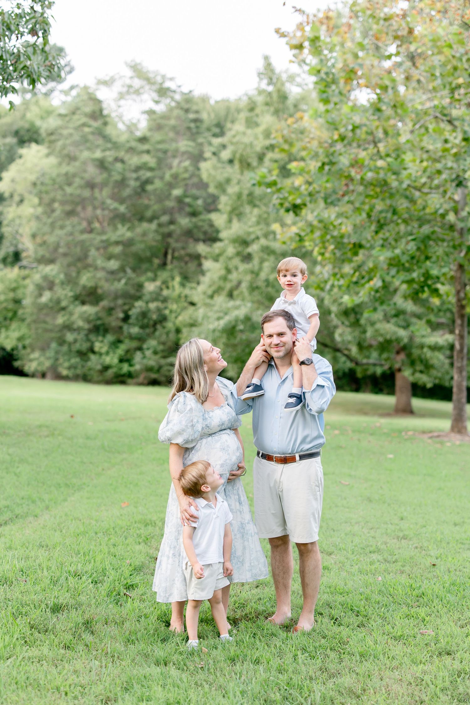 A family shares a joyful moment together on a grassy lawn with trees in the background.