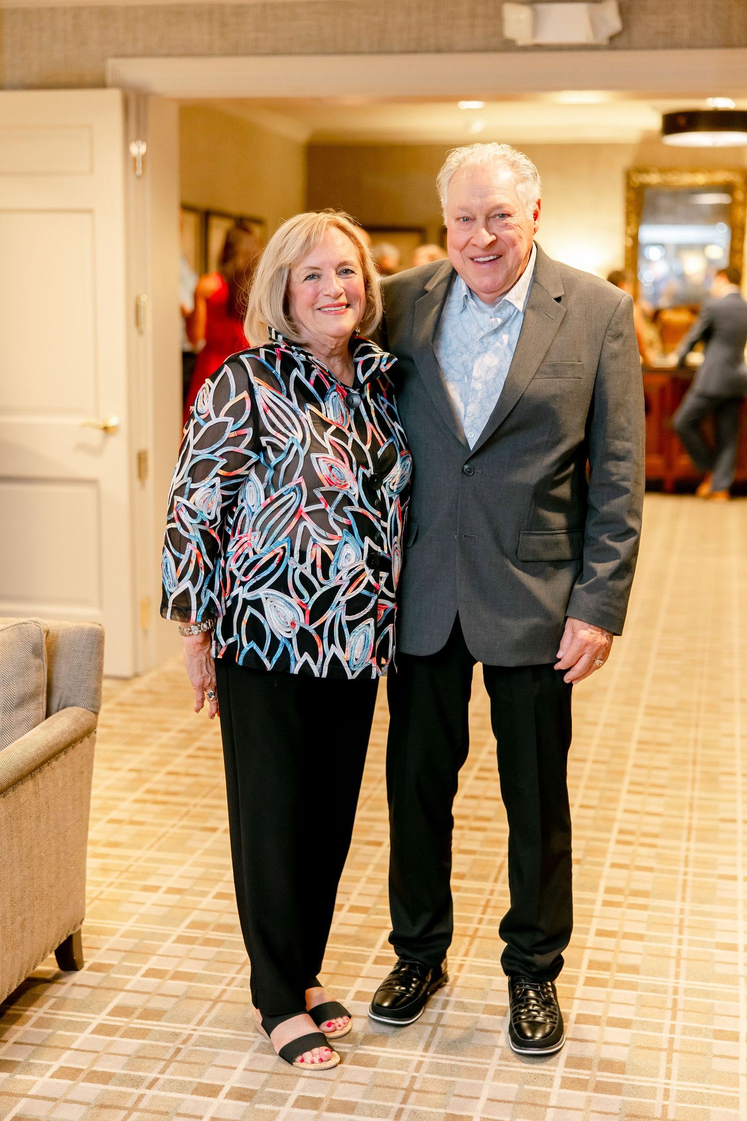 A couple poses together in formal attire on a tiled floor in an indoor venue.
