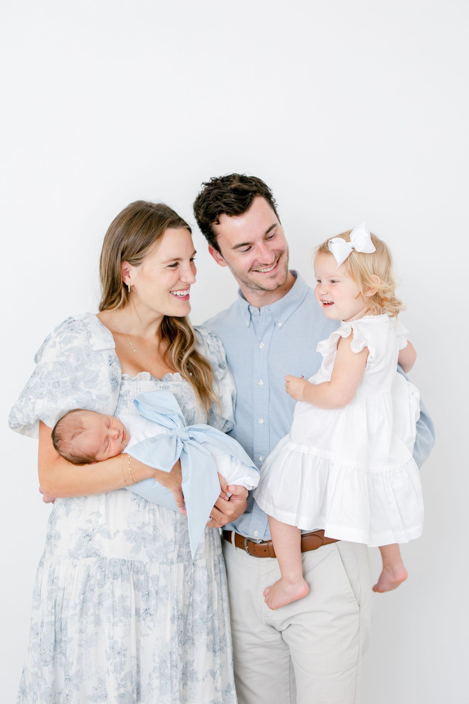 A family wearing light blue and white outfits poses together in a series of four connected studio portraits.