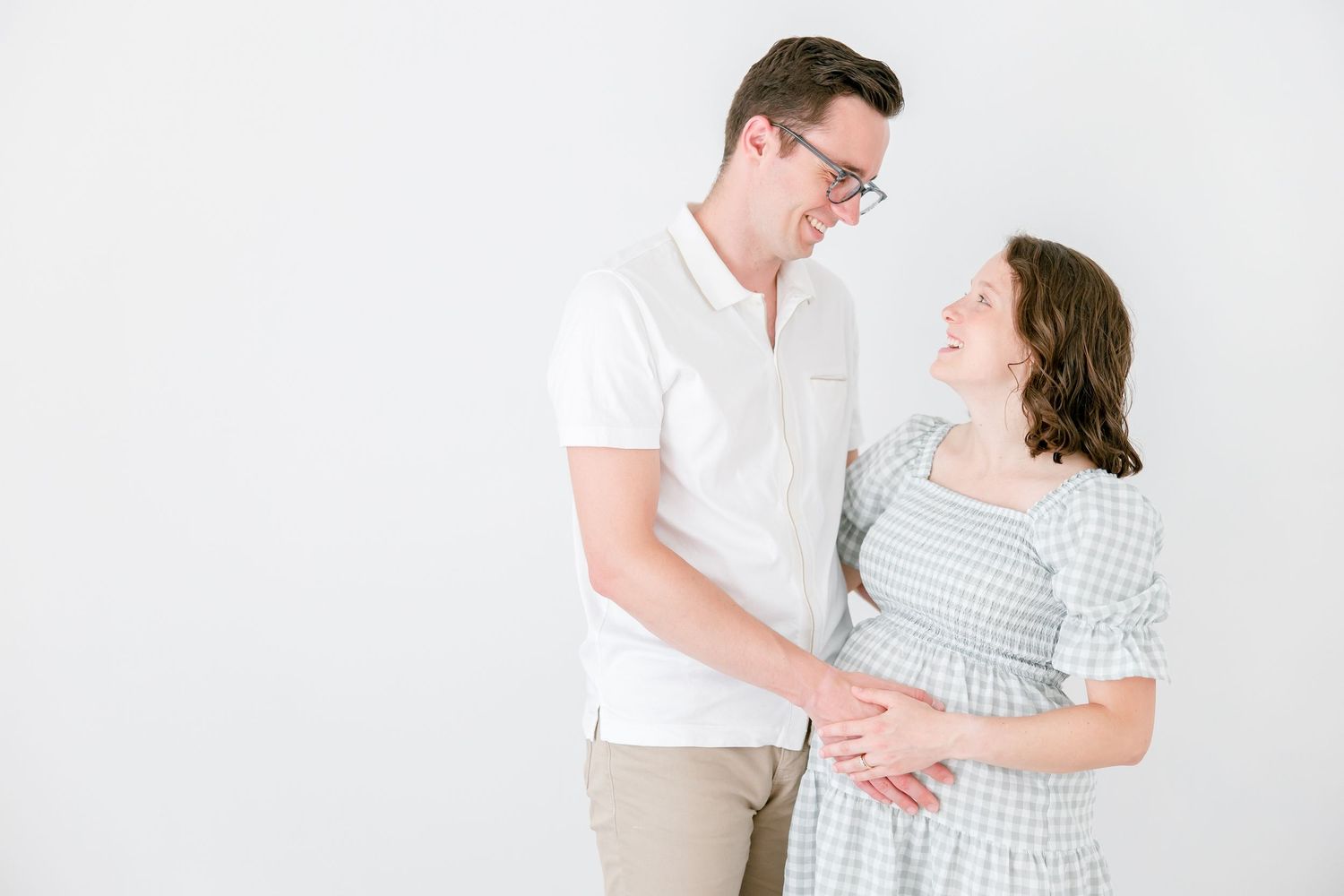 A couple in casual white and blue outfits share a tender moment against a white backdrop during a photo session.
