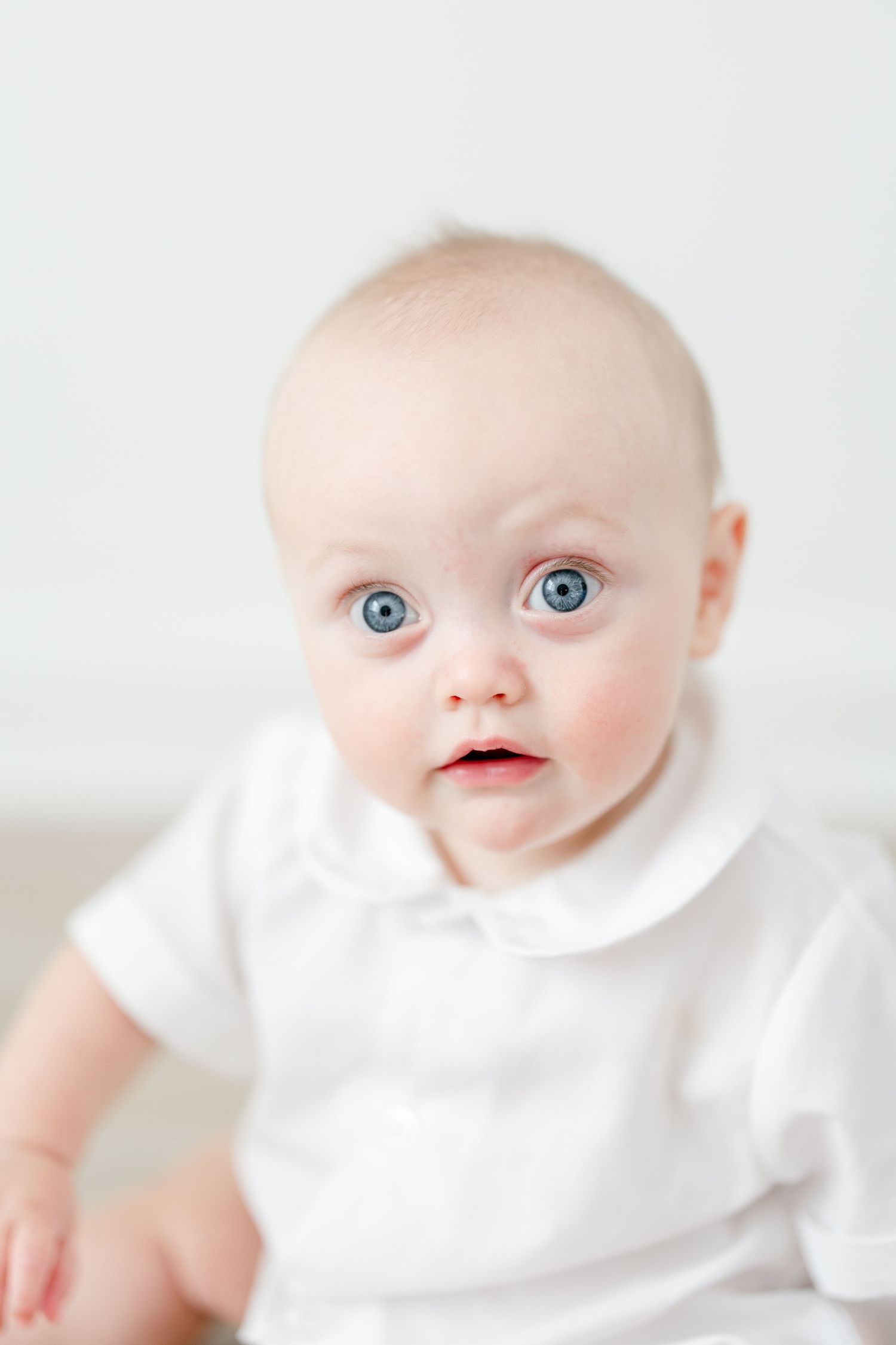 Close up portrait of baby in white outfit against bright white background.