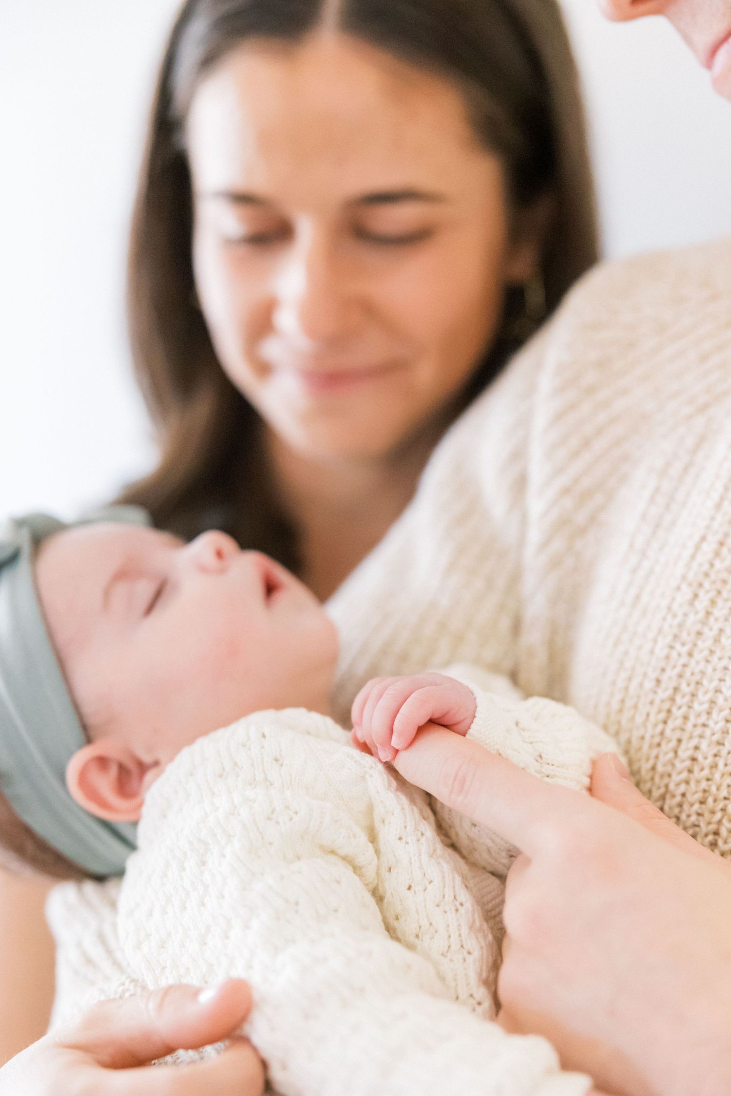 Tender moment with sleeping baby in cream sweater and mint bow headband being held.