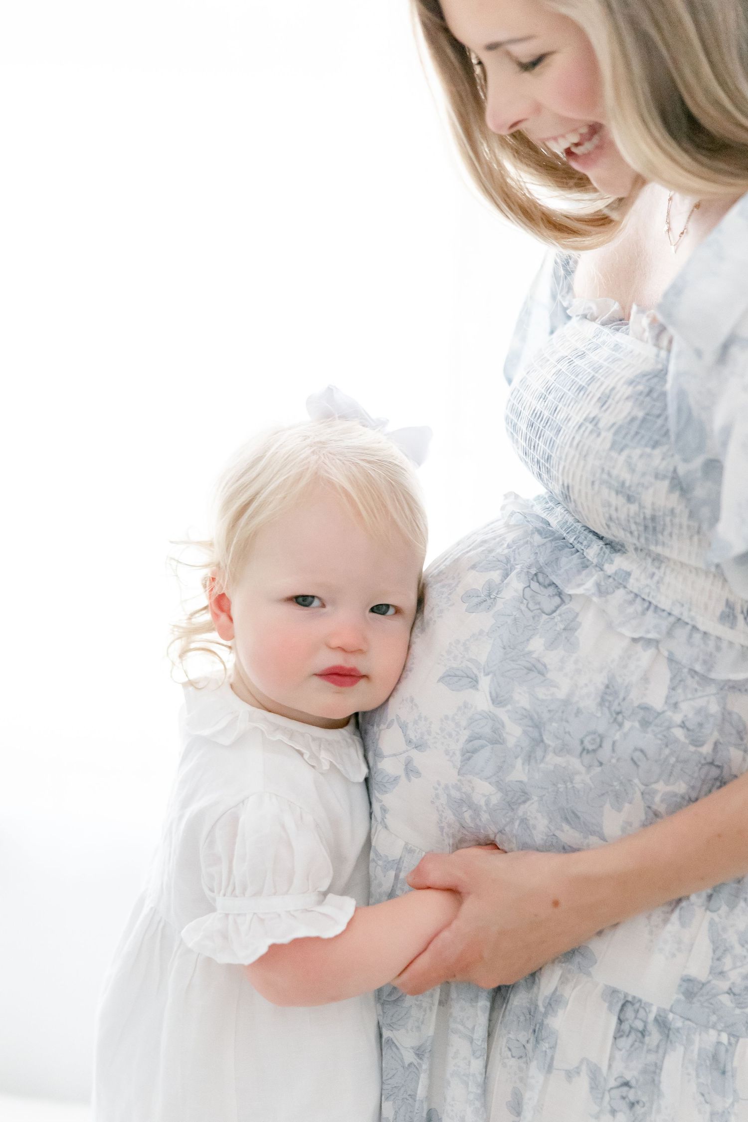 A bright and airy maternity portrait showing a sweet moment between parent and young child.