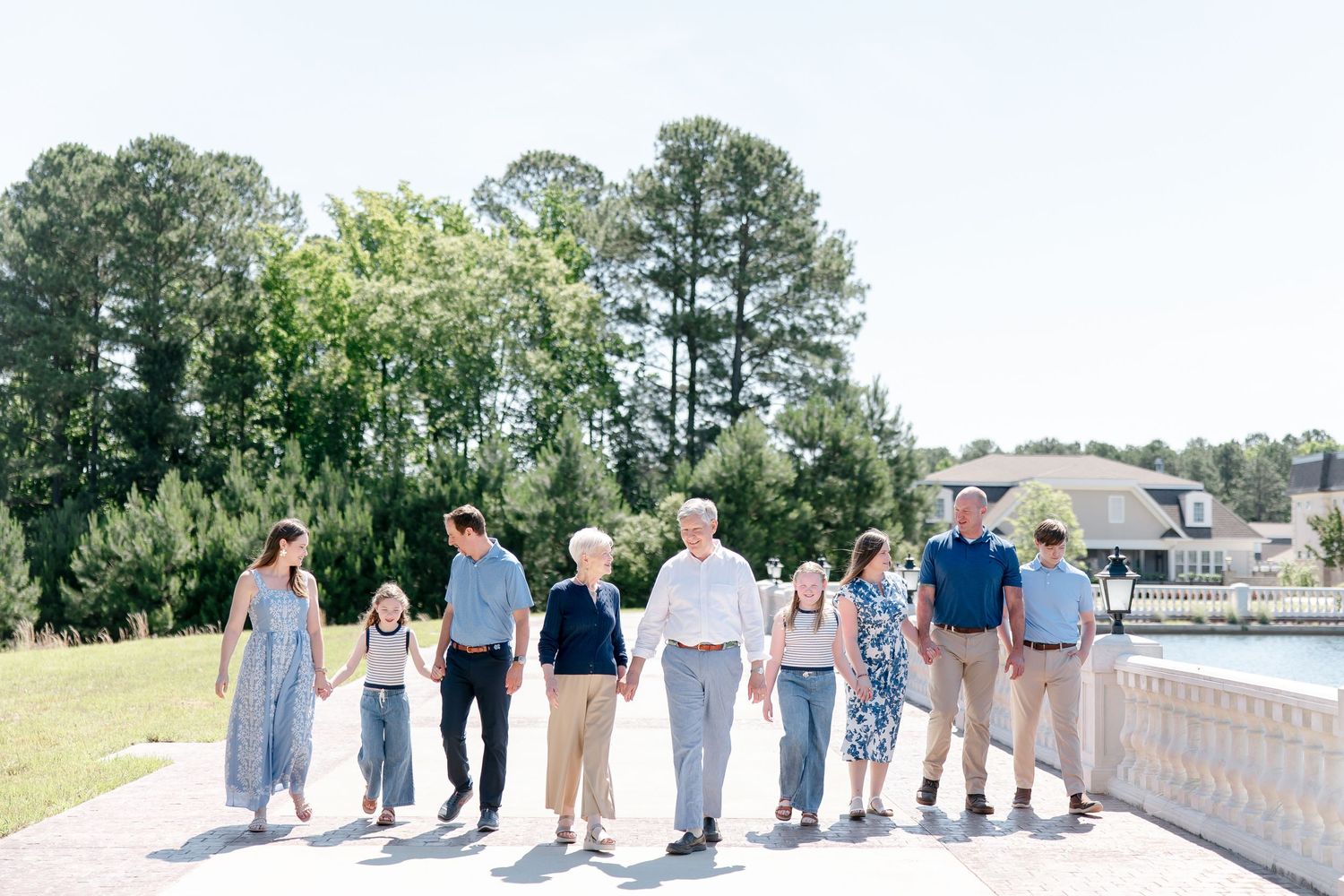 Group of people walking together along a waterfront path with trees and railings in a panoramic sequence.