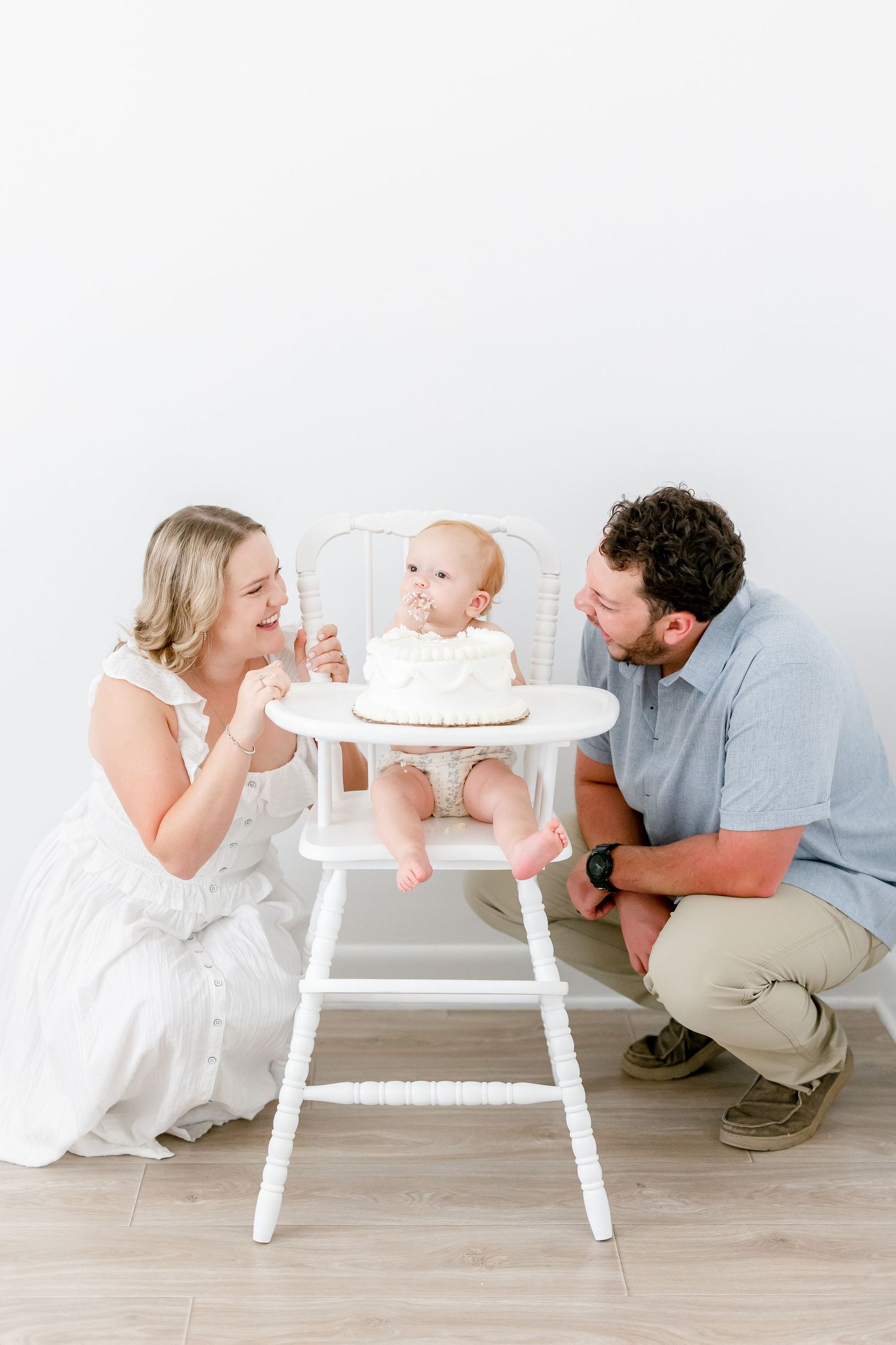 Modern minimalist family photo scene in white with tiny cake on high chair.