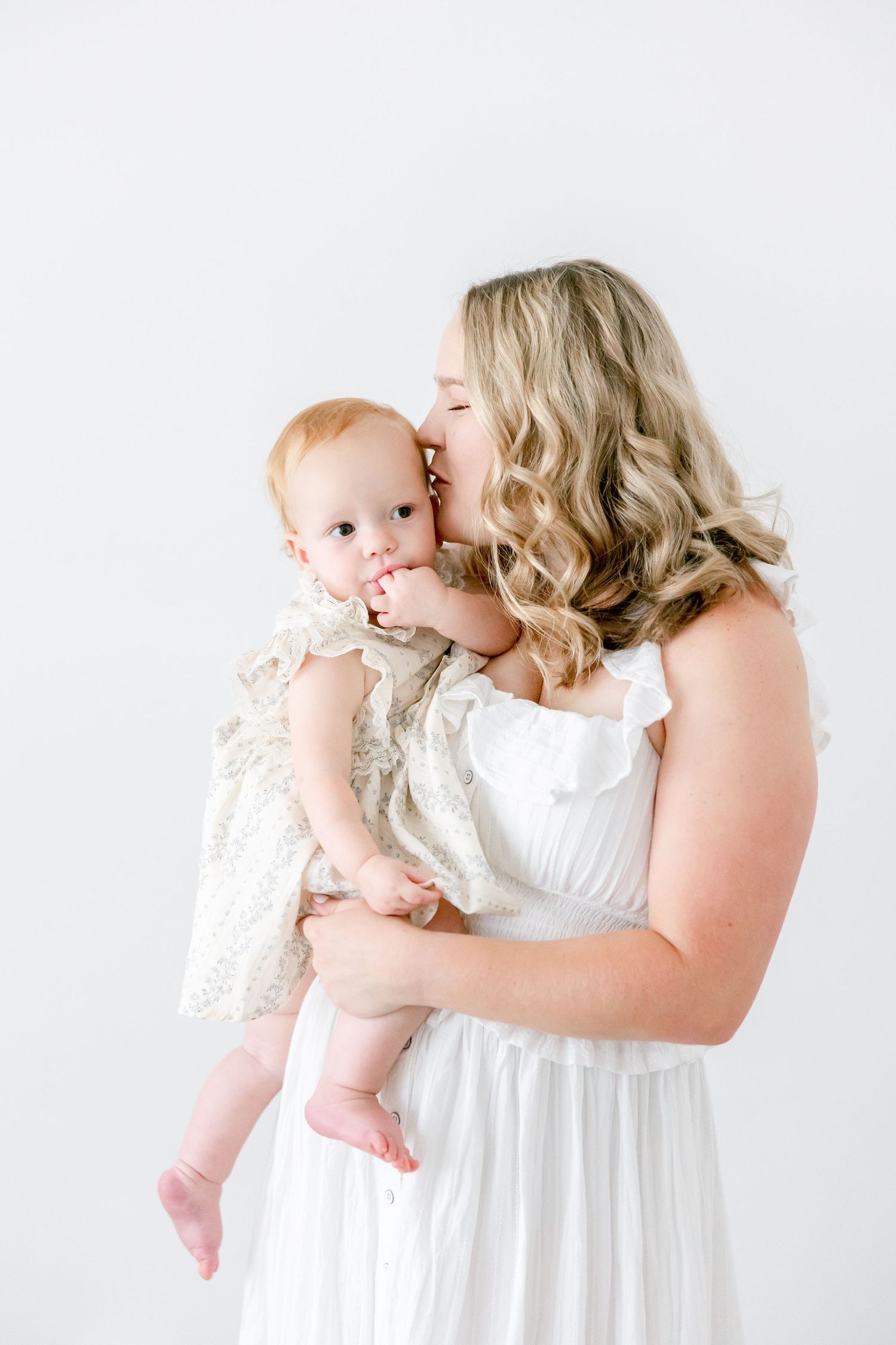 A tender moment captured in white as a parent in a flowing dress lovingly embraces their baby in delicate lace.