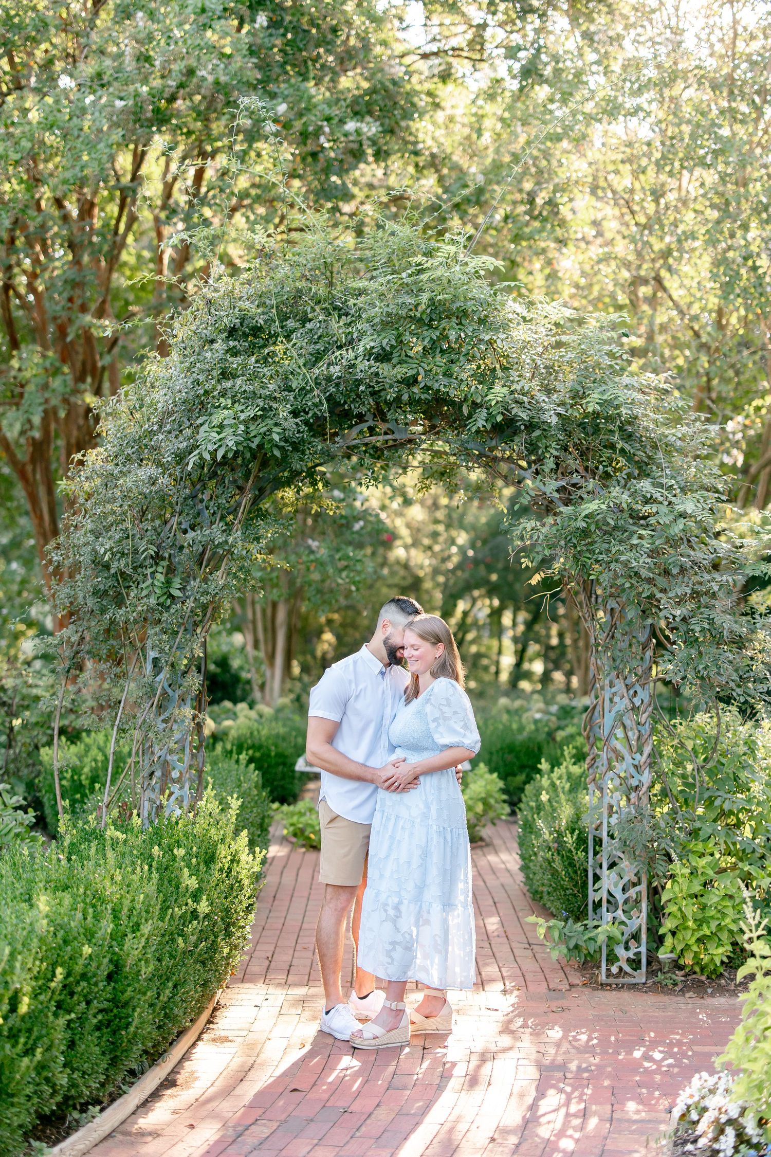 Couple sharing intimate moments under a flowering garden arbor on a brick pathway.