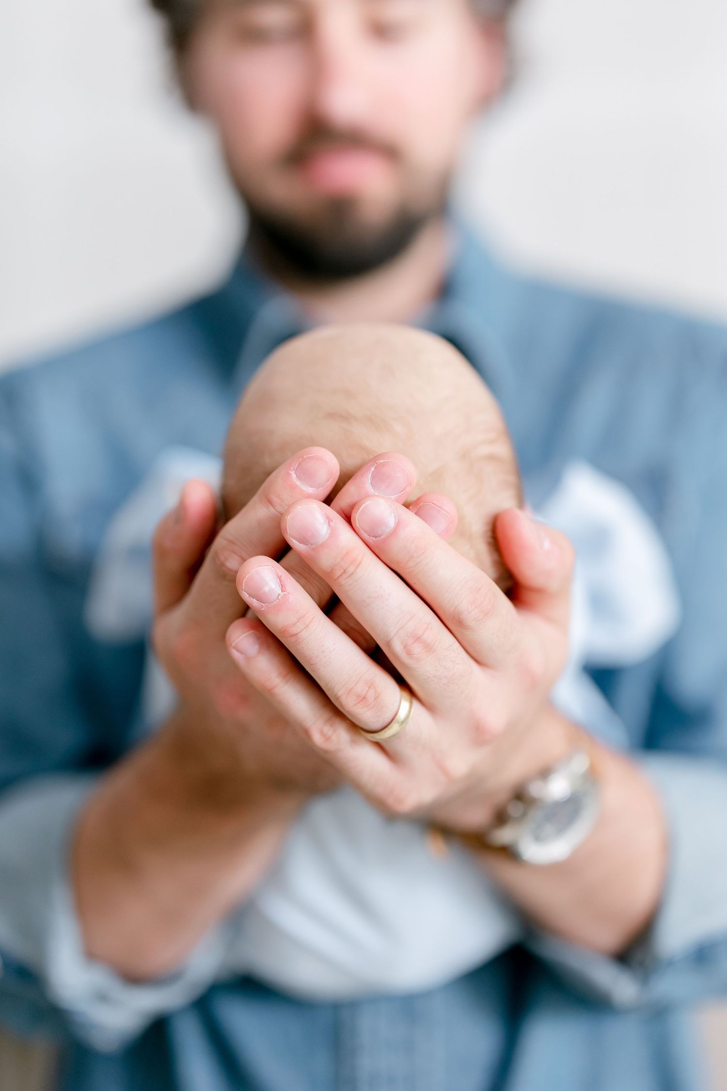 Close-up of hands gently cradling sleeping newborn baby against denim shirt.