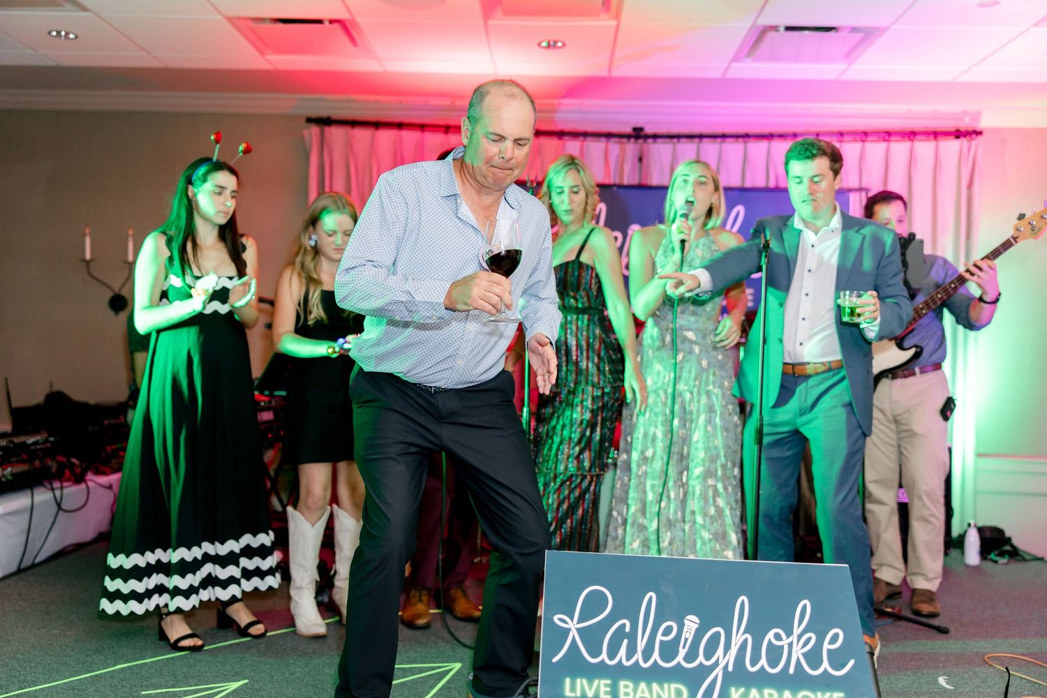 Party guests dancing and celebrating at an event with colorful lighting and a 'Lakechoke' sign visible.