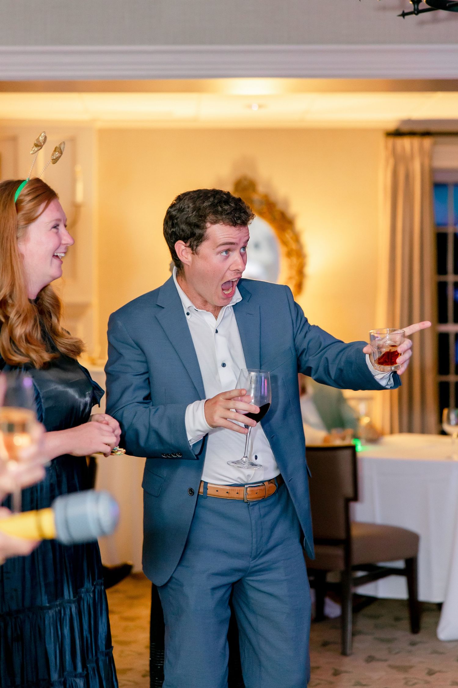 People dancing and celebrating at an indoor event with wine glasses in an elegant room setting.