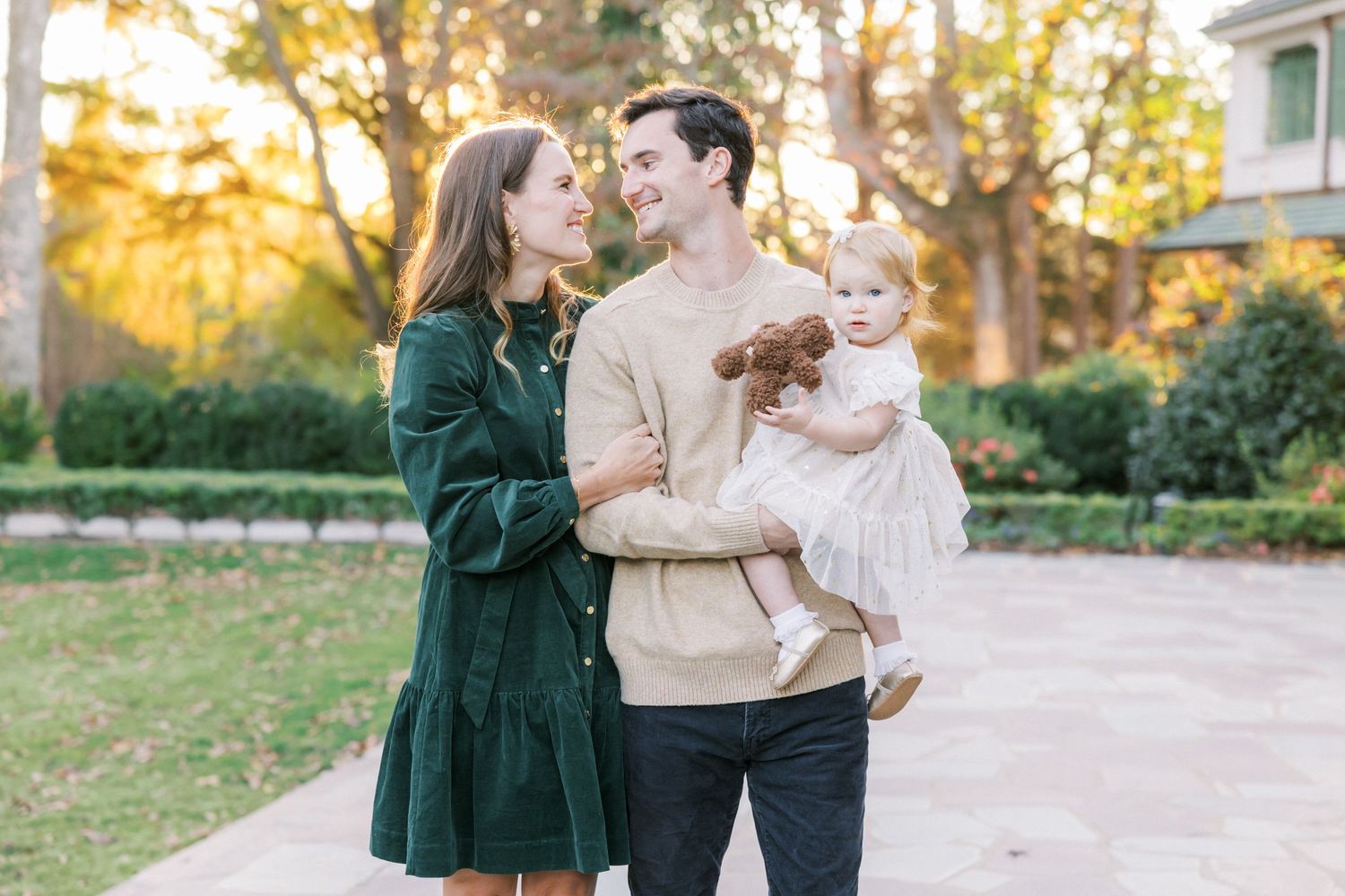 A couple in casual fall attire shares a loving moment with their baby outdoors during golden hour.