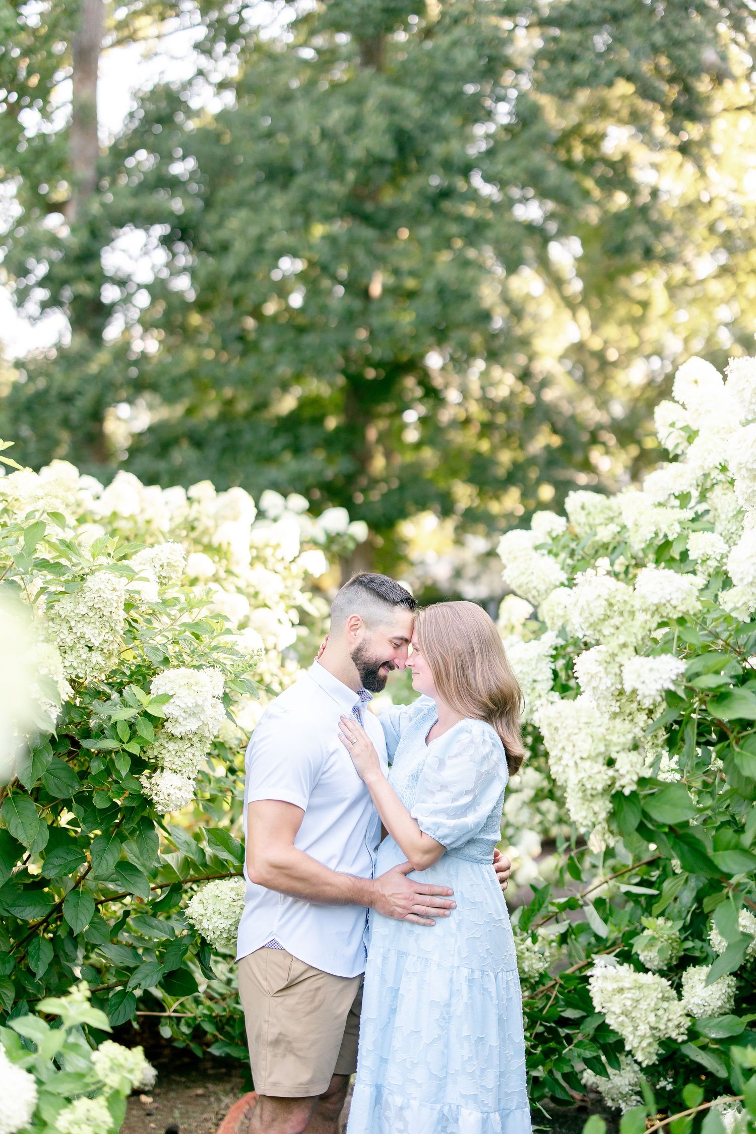 Couple shares intimate moment among blooming white hydrangea bushes in garden setting.