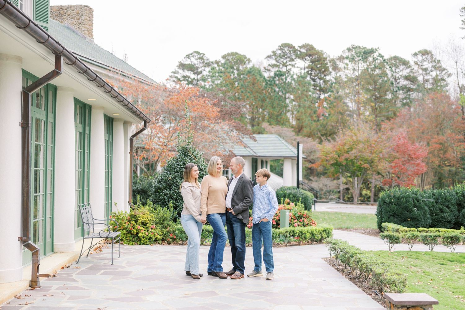 People walking together on a garden path beside a white building with fall foliage and trees in the background.