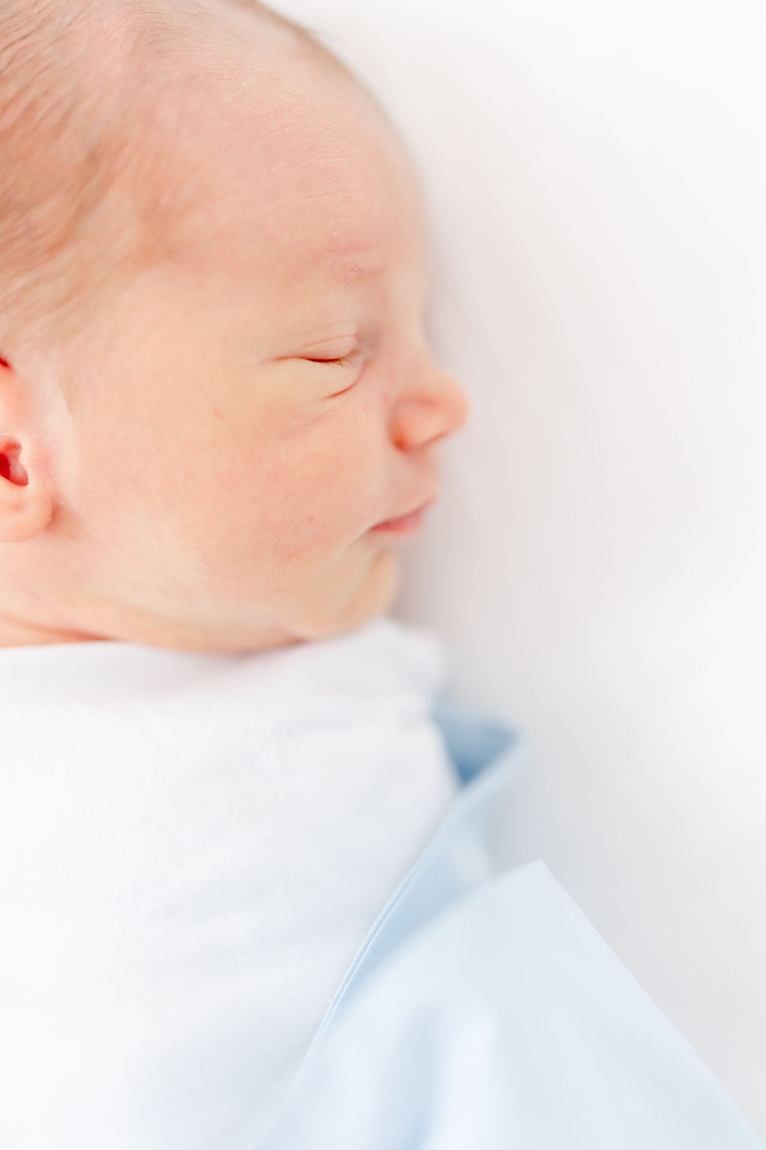 A peaceful sleeping newborn baby swaddled in soft light blue blanket against white background.