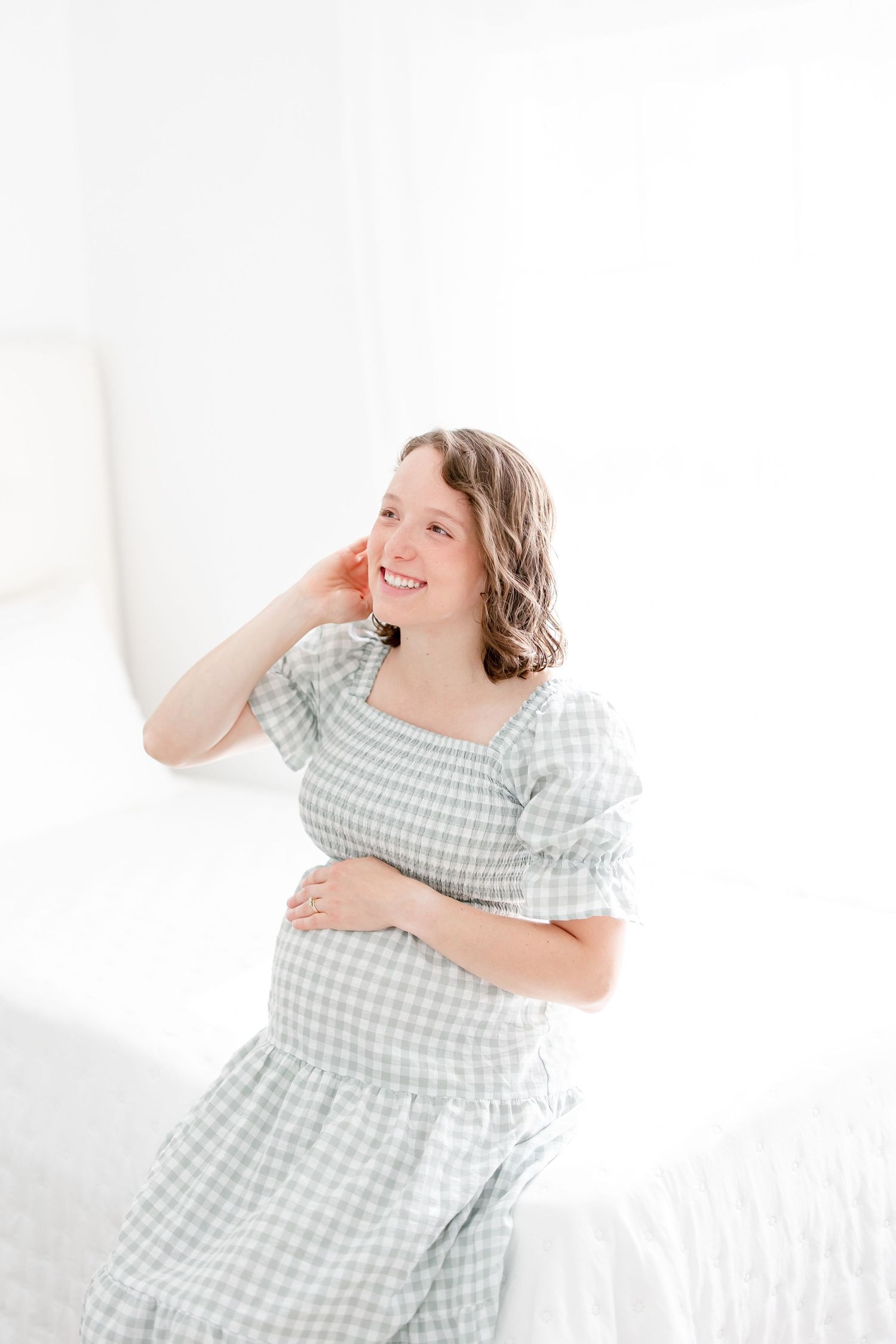 A person in a light blue gingham dress laughs joyfully while posing against a bright white background.