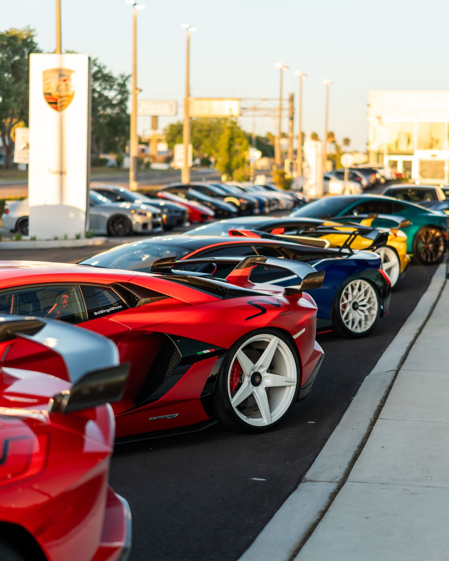 Lineup of exotic cars and Lamborghinis parked outside a dealership at sunset