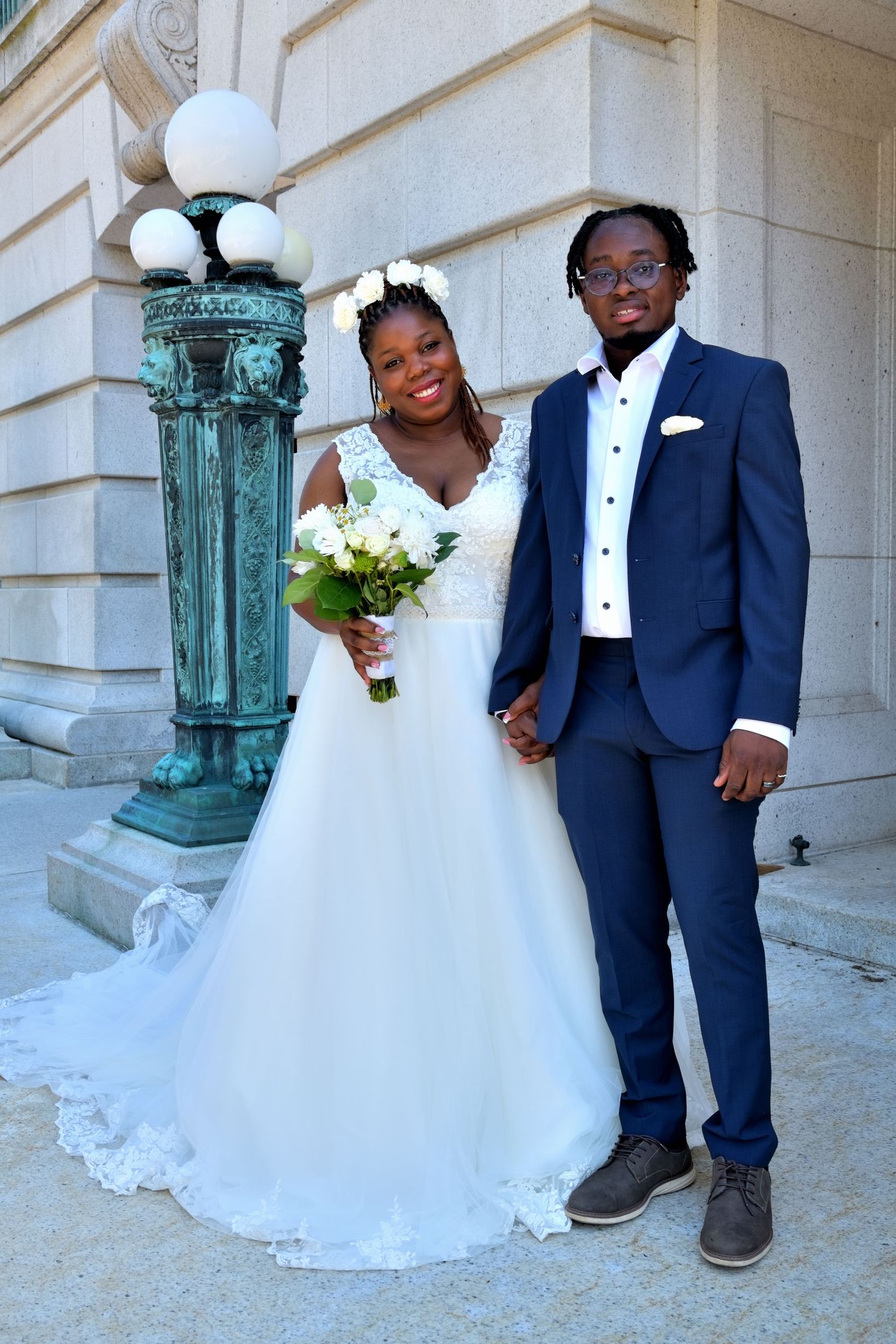 Bride and groom pose together in wedding attire beside vintage green lamp post outdoors.