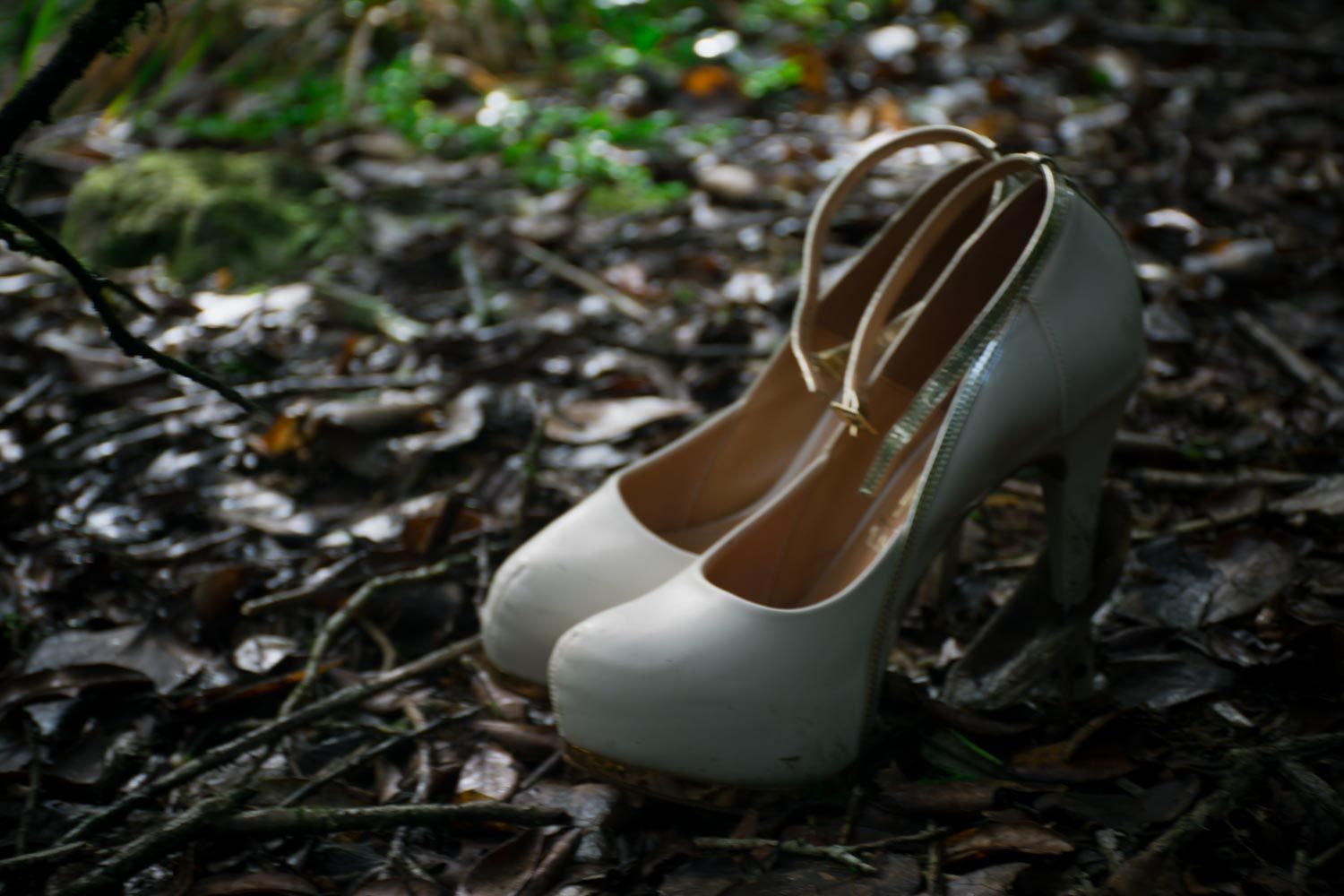 White platform high heel bridal shoes placed on a forest floor covered with leaves.
