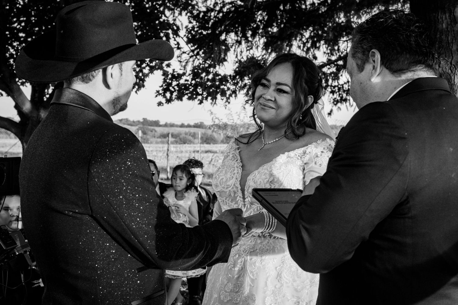 Black and white close-up of smiling bride exchanging rings with groom during outdoor wedding ceremony.