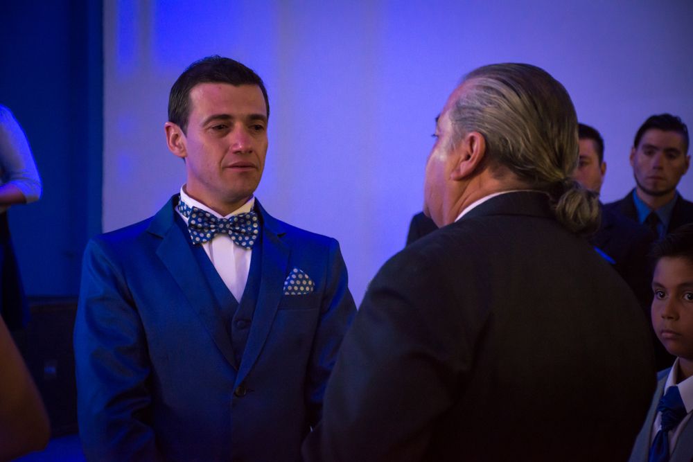 Young man in blue suit with polka dot bow tie conversing with older gentleman at wedding reception.