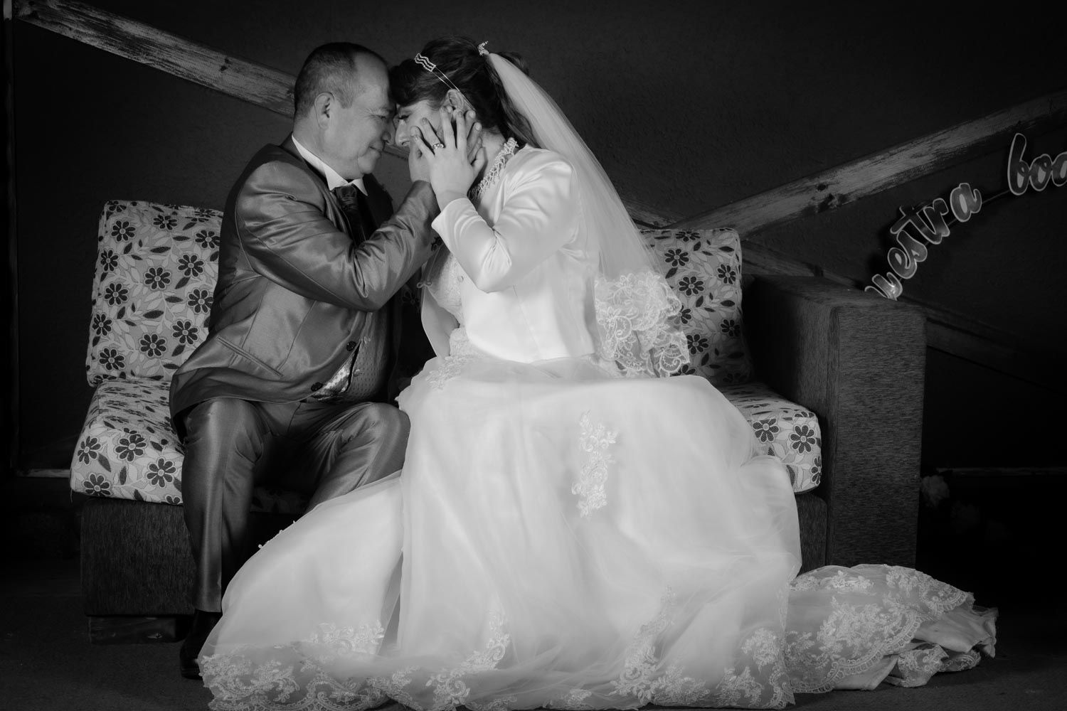 Black and white romantic wedding photo of groom tenderly touching brides face on sofa.