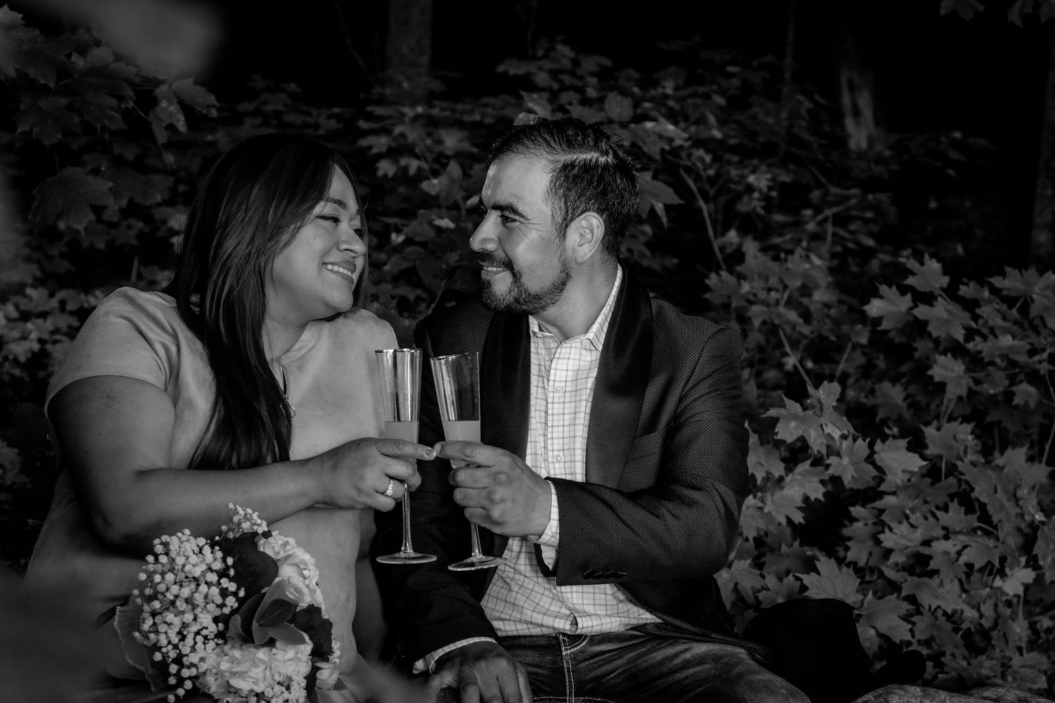 Black and white photo of a smiling couple toasting with champagne glasses during outdoor celebration.