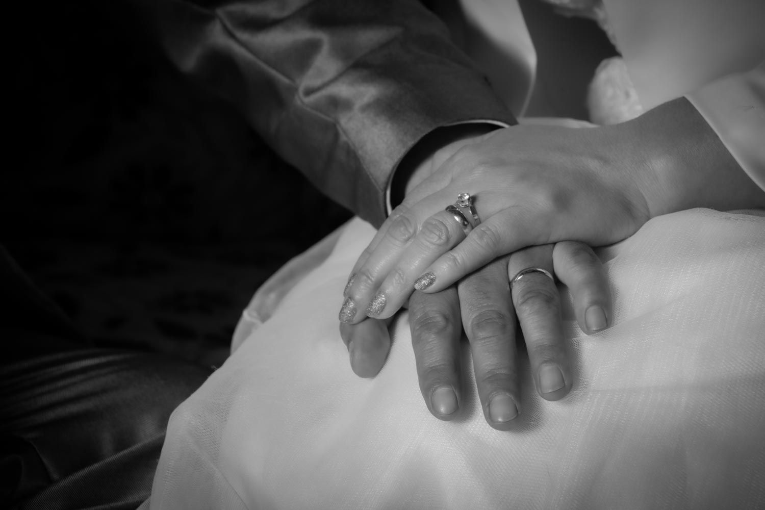 Close-up black and white photo of bride and grooms hands with wedding rings intertwined.