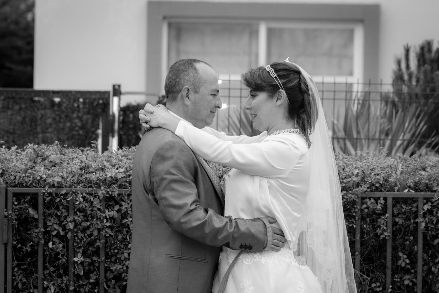 Black and white photo of bride and groom embracing tenderly outside near garden fence.