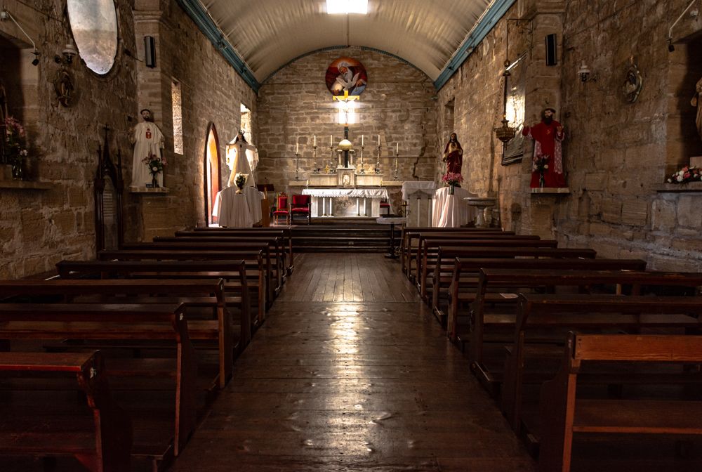 Interior of a historic stone church with wooden pews, vaulted ceiling, and illuminated altar.
