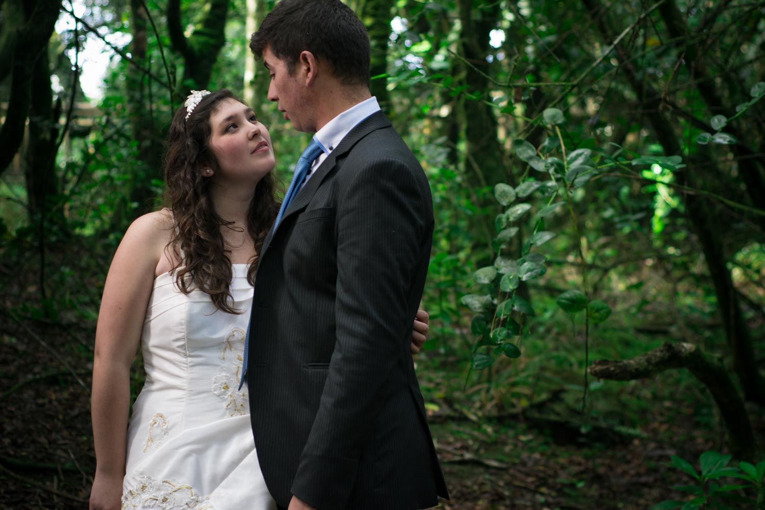 Bride and groom share an intimate moment standing together in a lush green forest.