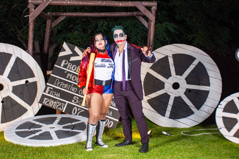 Couple dressed as Joker and Harley Quinn posing at an outdoor Halloween costume party.