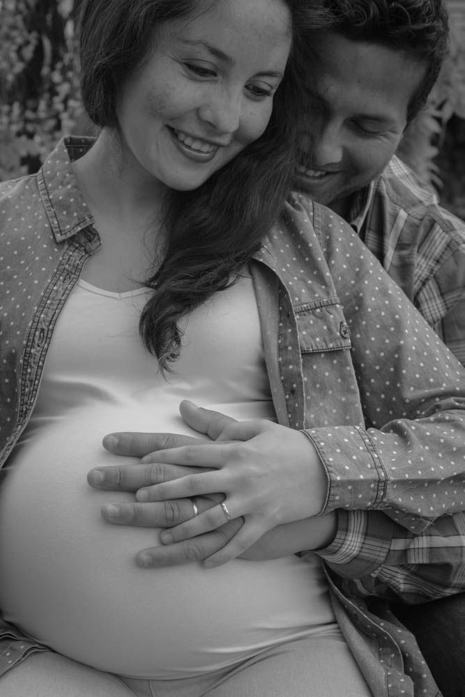 Happy expecting couple smiling as man embraces pregnant woman's belly in black and white photo.