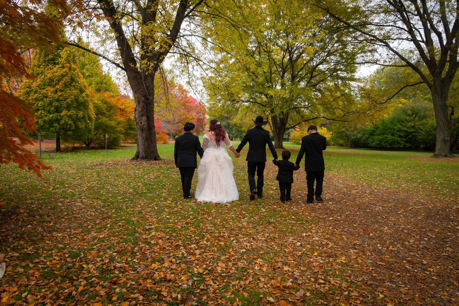 Wedding party walking through colorful autumn park with fallen leaves on the ground.