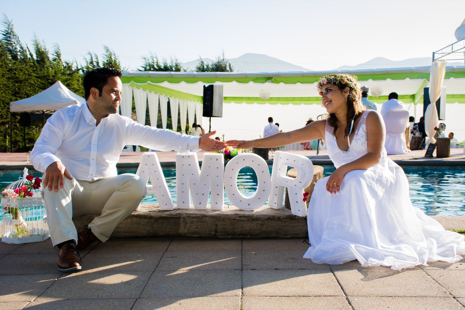 Bride and groom posing beside large AMOR letters near a pool at their wedding.