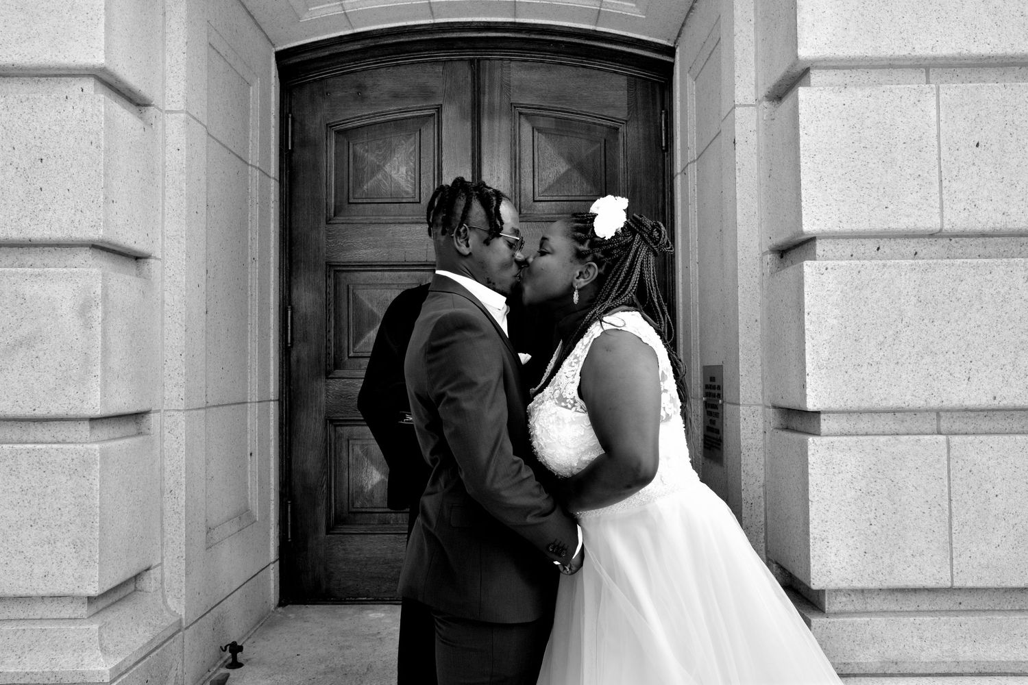 Newlyweds share romantic black and white kiss in front of ornate wooden doors.