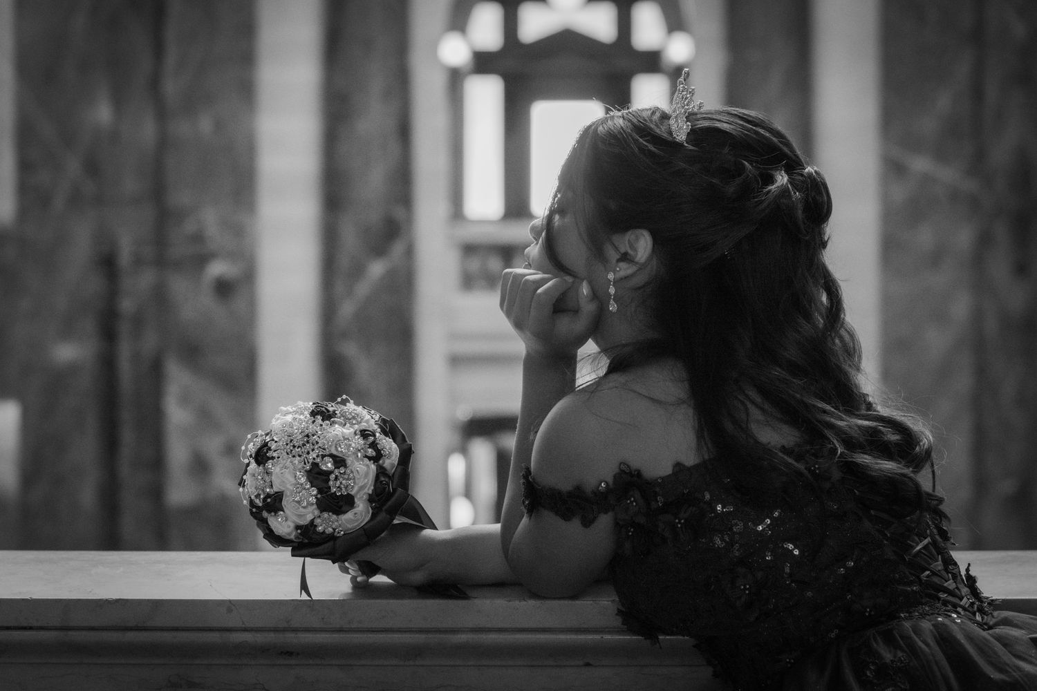 Black and white portrait of young woman holding bouquet in elegant formal setting.
