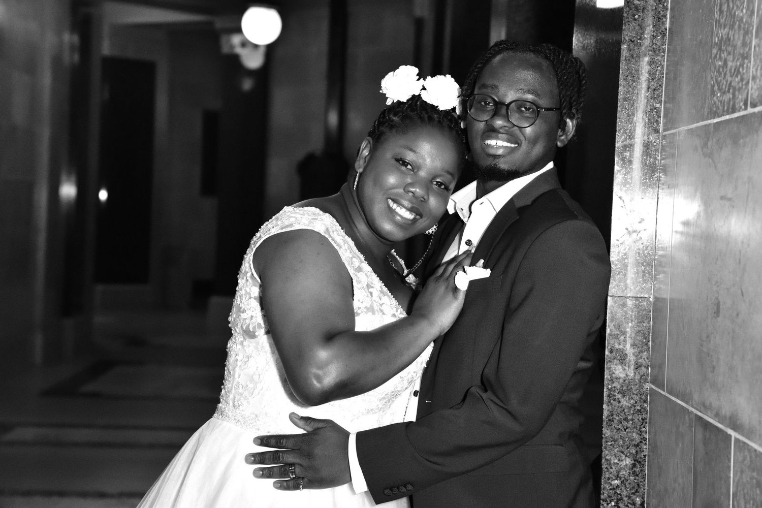 A Black bride and groom share a joyful embrace in a black and white wedding portrait in a classic hall.