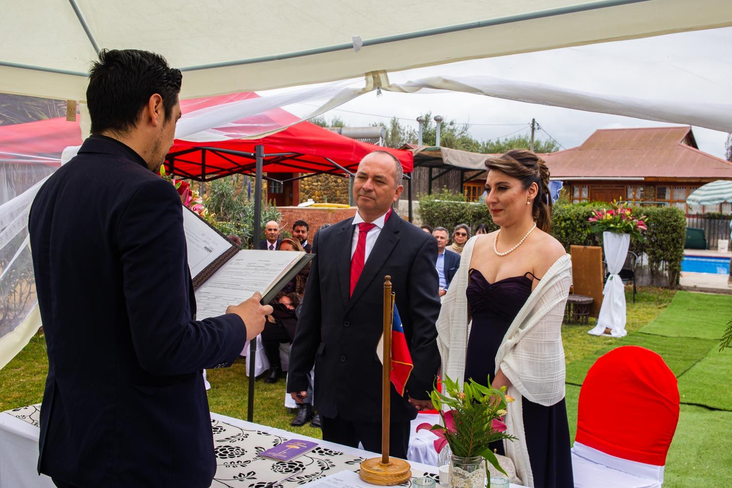 Officiant reading vows to couple during an outdoor wedding ceremony under a tent.