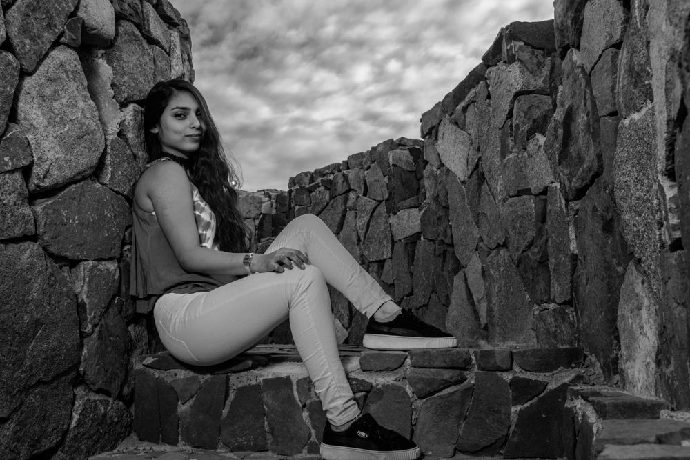 Young woman in casual outfit posing on stone steps in a black and white portrait.