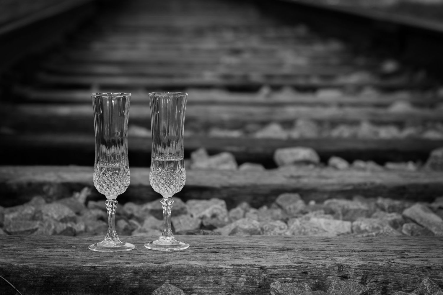 Two crystal champagne flutes placed on wooden railroad ties in elegant black and white wedding photo.