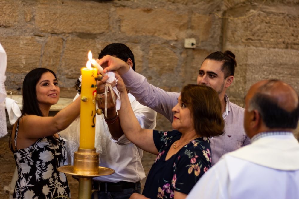 Group of people lighting a large candle together during a religious ceremony in a stone church.
