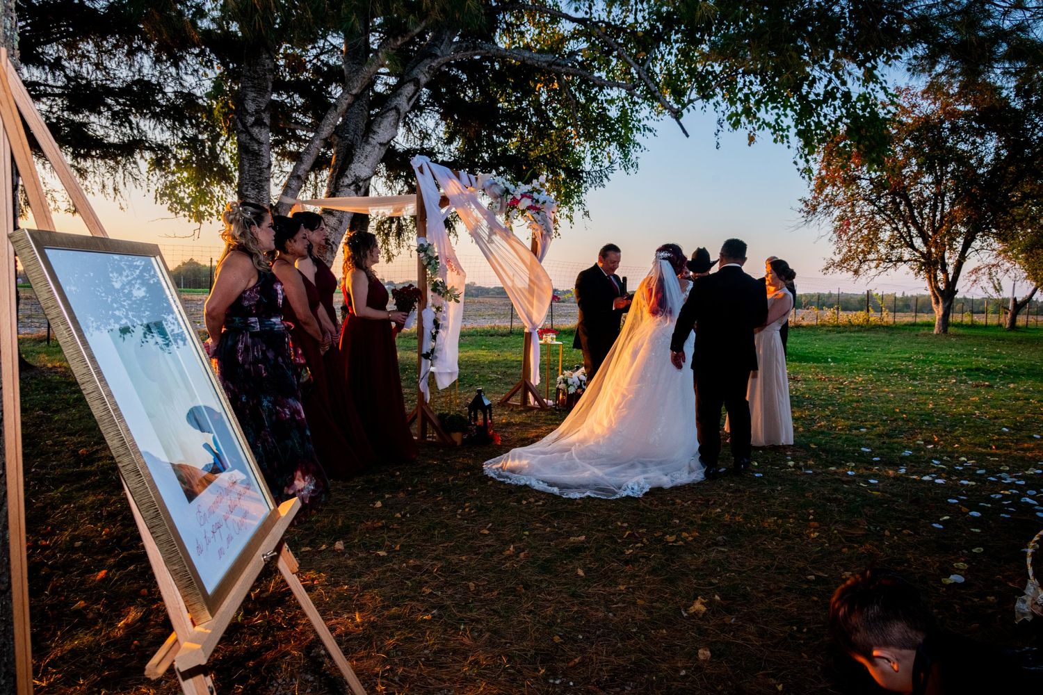 Romantic outdoor wedding ceremony at sunset with decorative arch, floral arrangements, and wedding party.
