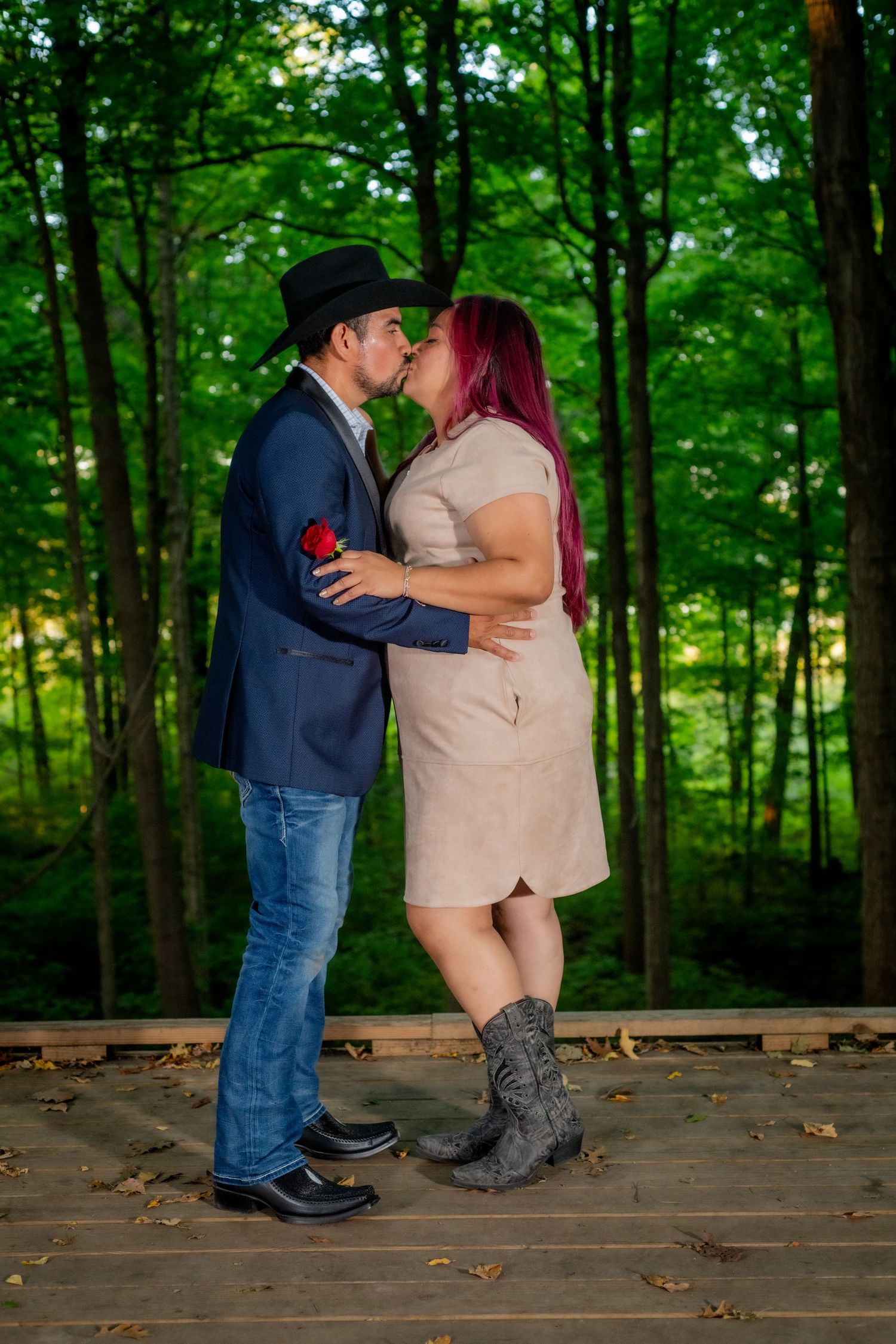 Couple sharing romantic kiss on wooden deck surrounded by lush green forest trees.