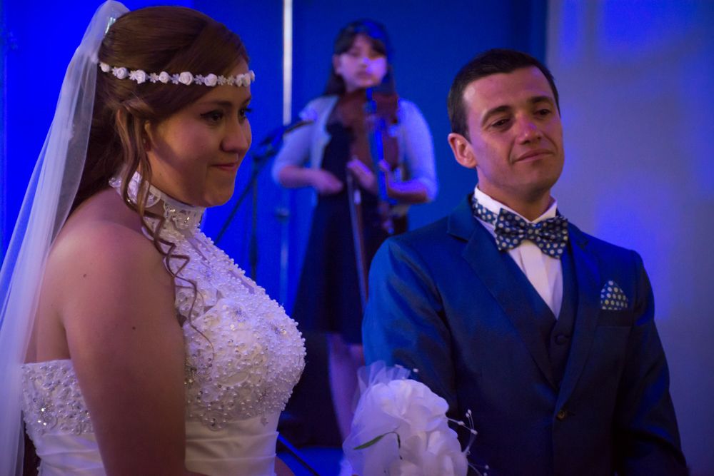 Bride in white gown with headpiece stands beside groom in blue suit during wedding ceremony.