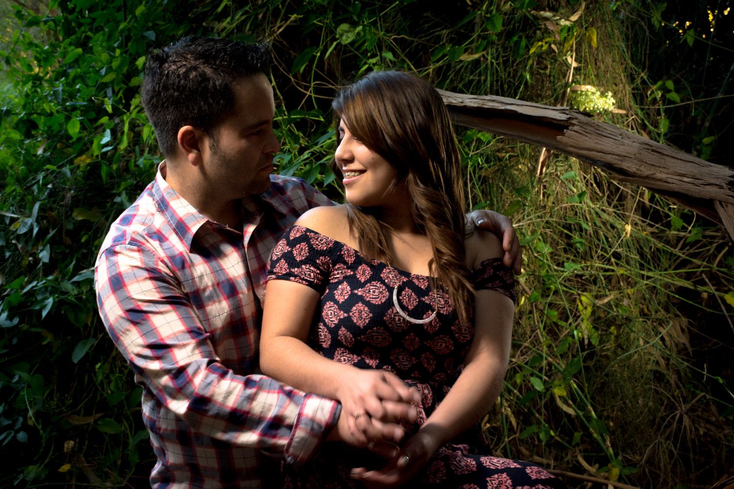 Loving couple embracing and smiling at each other surrounded by vibrant green vegetation.