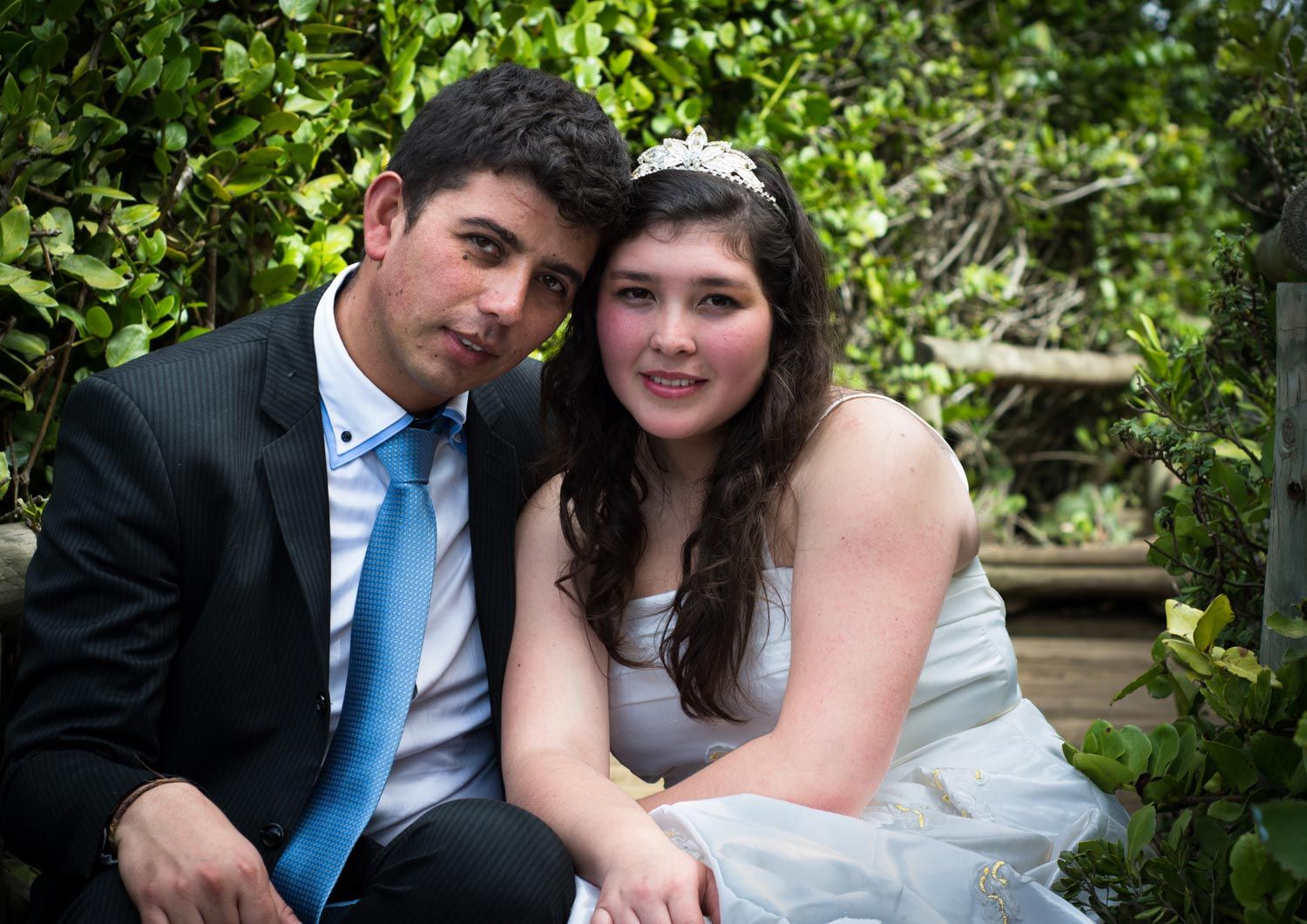 Newlywed couple smiling and posing together surrounded by lush green foliage after wedding.