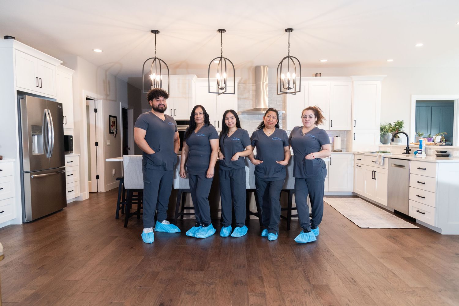 Team of five healthcare professionals in scrubs posing together in a modern white kitchen.