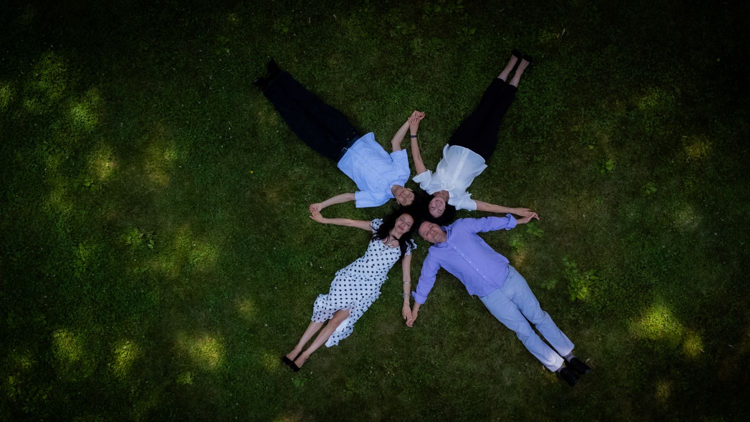 Aerial view of three people lying on green grass forming a star shape in a park.