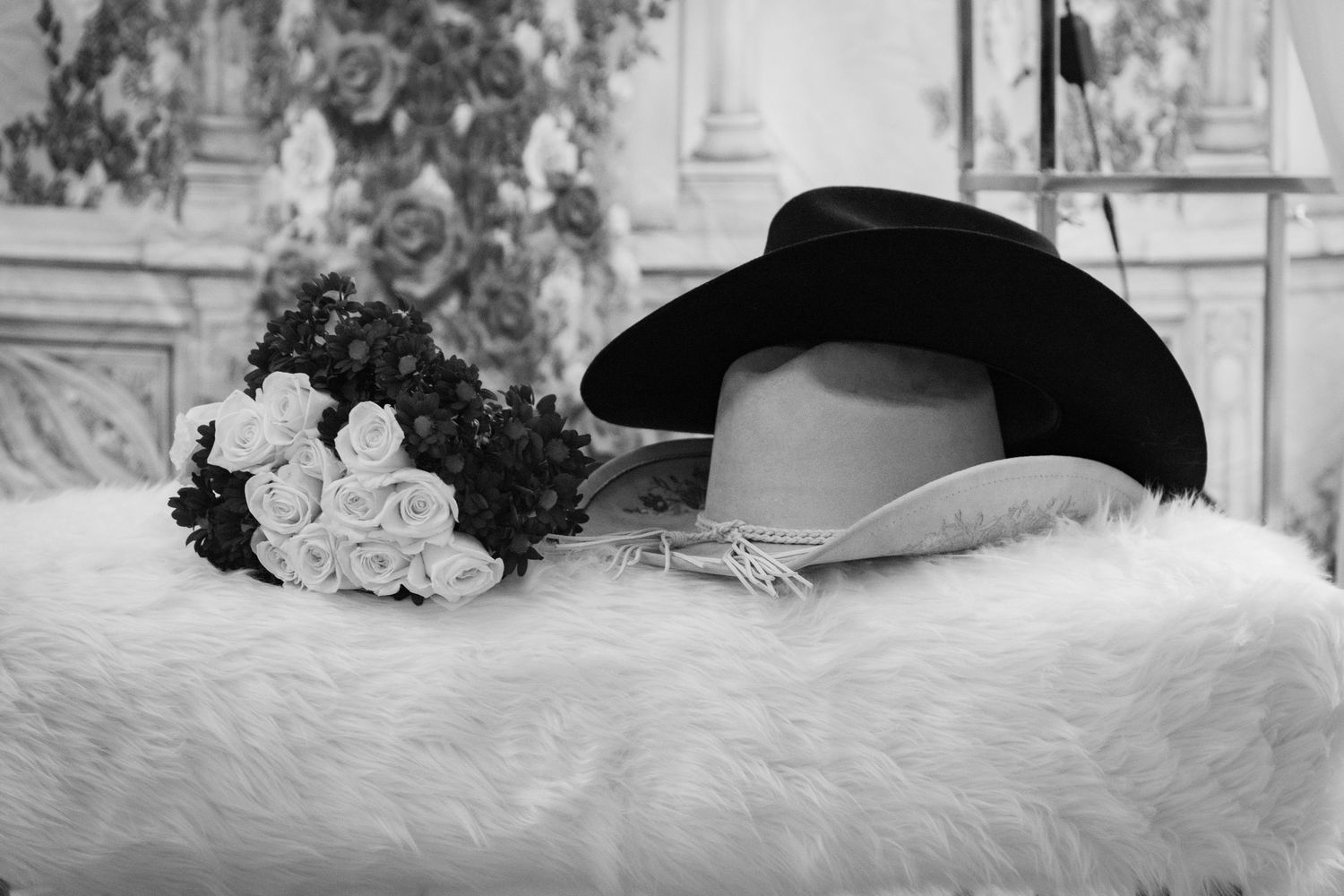 Black and white photo of a cowboy hat and floral bouquet resting on a fluffy white surface at a wedding.